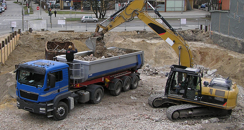 Ein LKW wird auf einer Baustelle von einem Bagger beladen